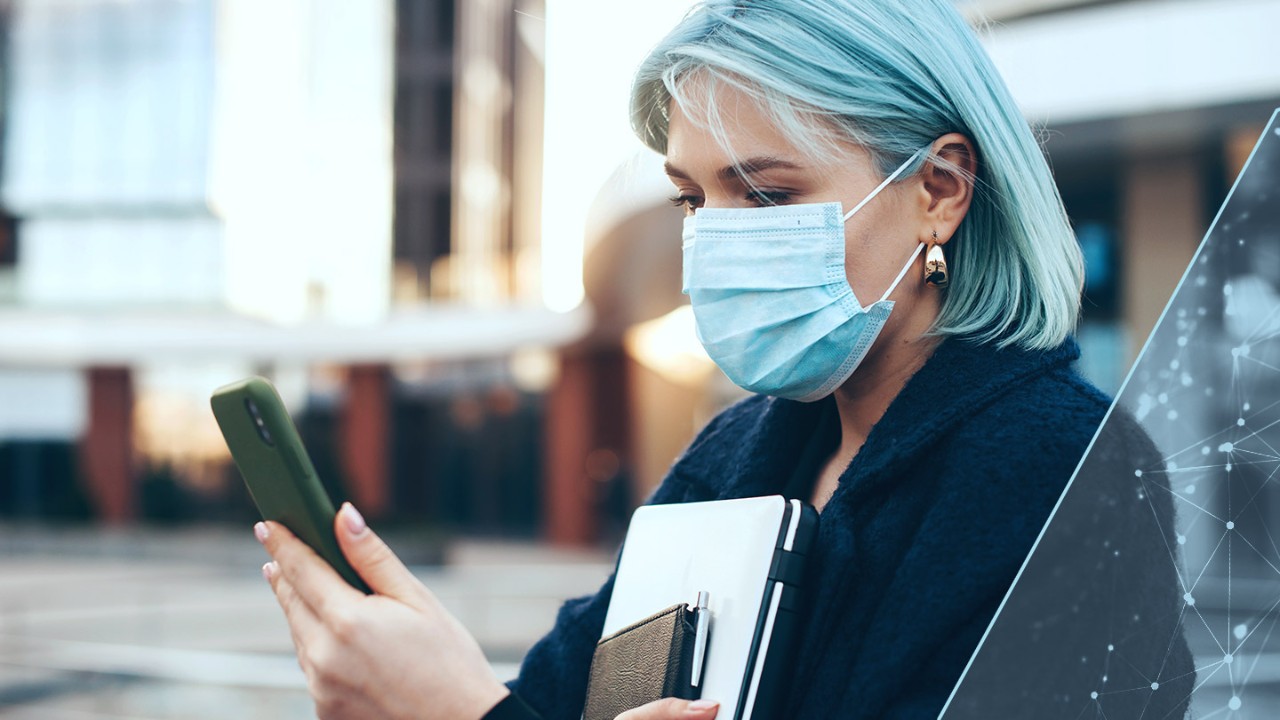 Woman outside in a protective mask holding and looking at her phone.