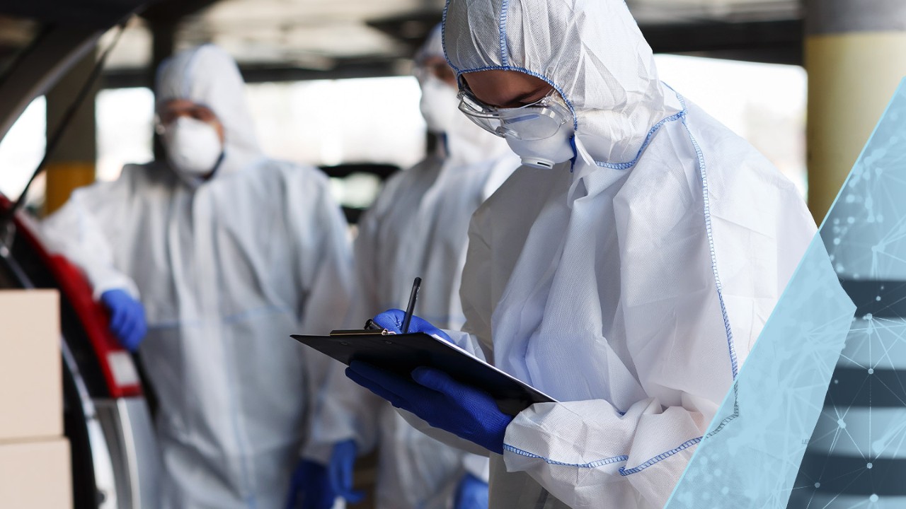 Three people in a warehouse wearing protective gear, with one person holding and writing on a clipboard.