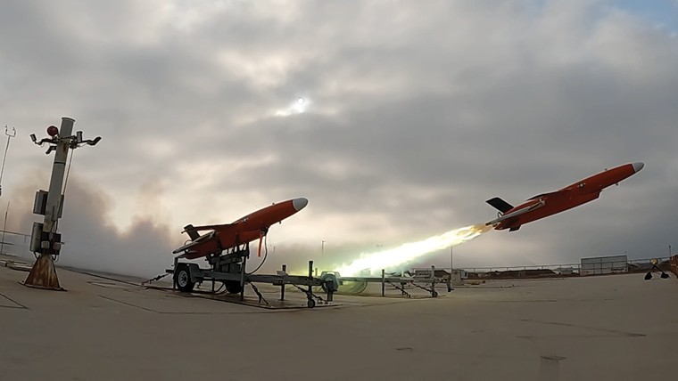 Two red drones launching from an airfield