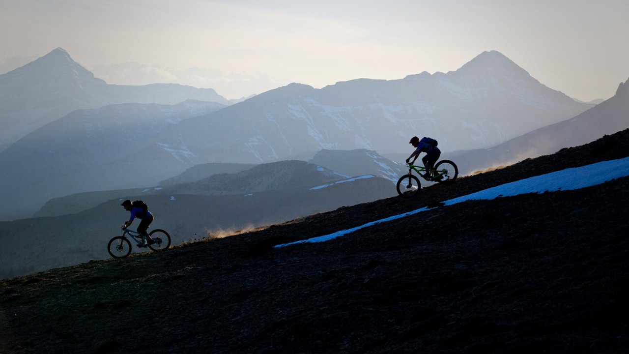 Two people riding mountain bikes down a mountain