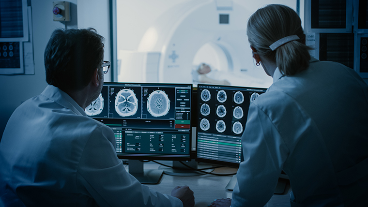 Two doctors looking at brain scans on desktop computers.