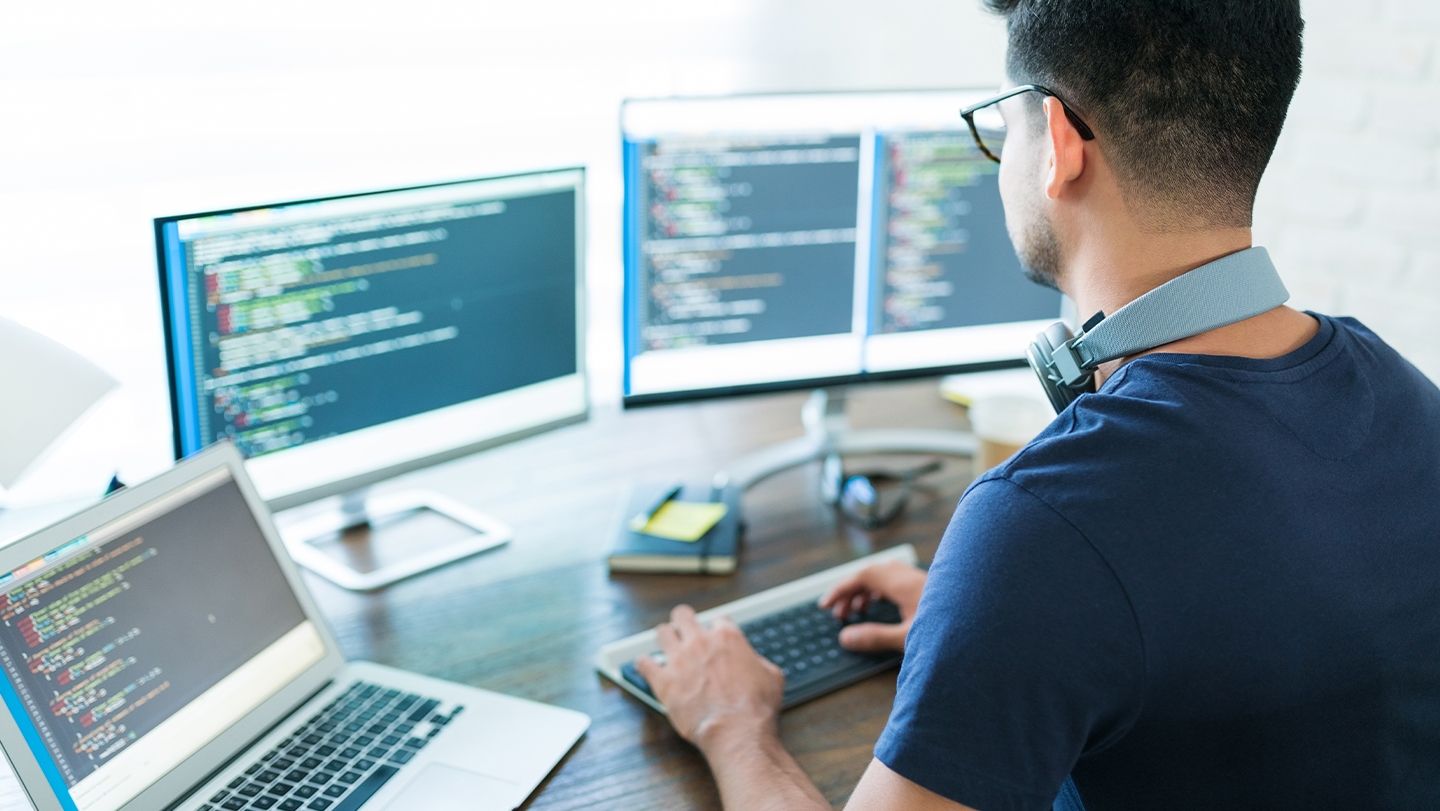 Man sitting at desk with multiple computer screens in front of him.