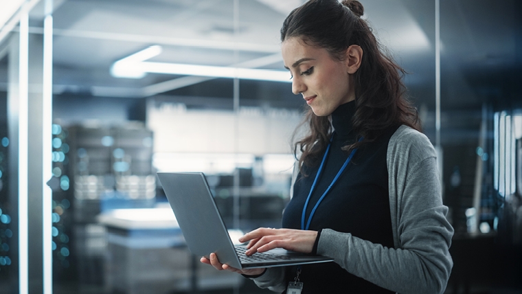 woman in work clothes standing with a laptop