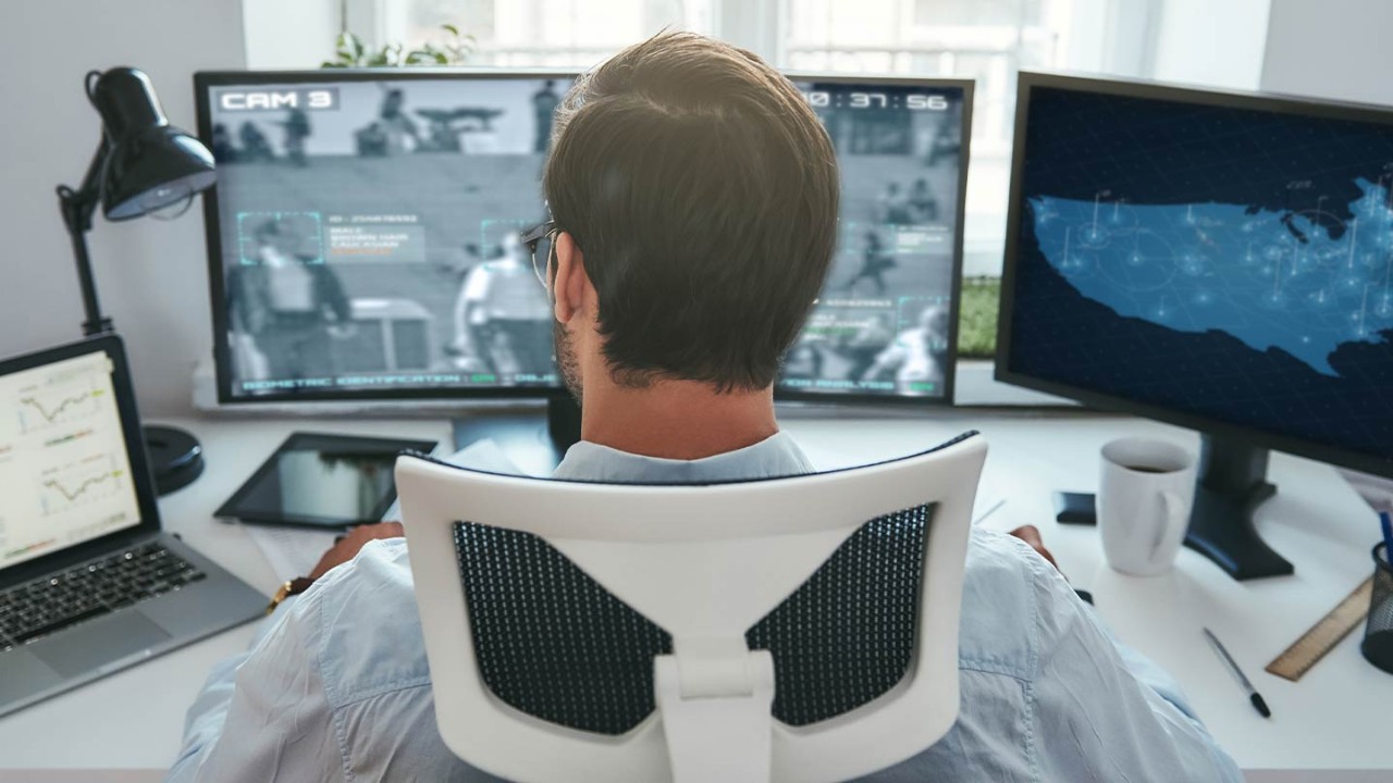 man at desk looks at camera tracking footage and a digital map of the United States