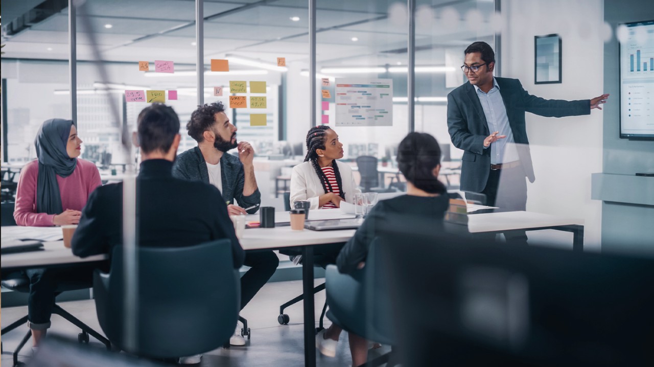 A multi-enthic team meets in a conference room to hear a presentation