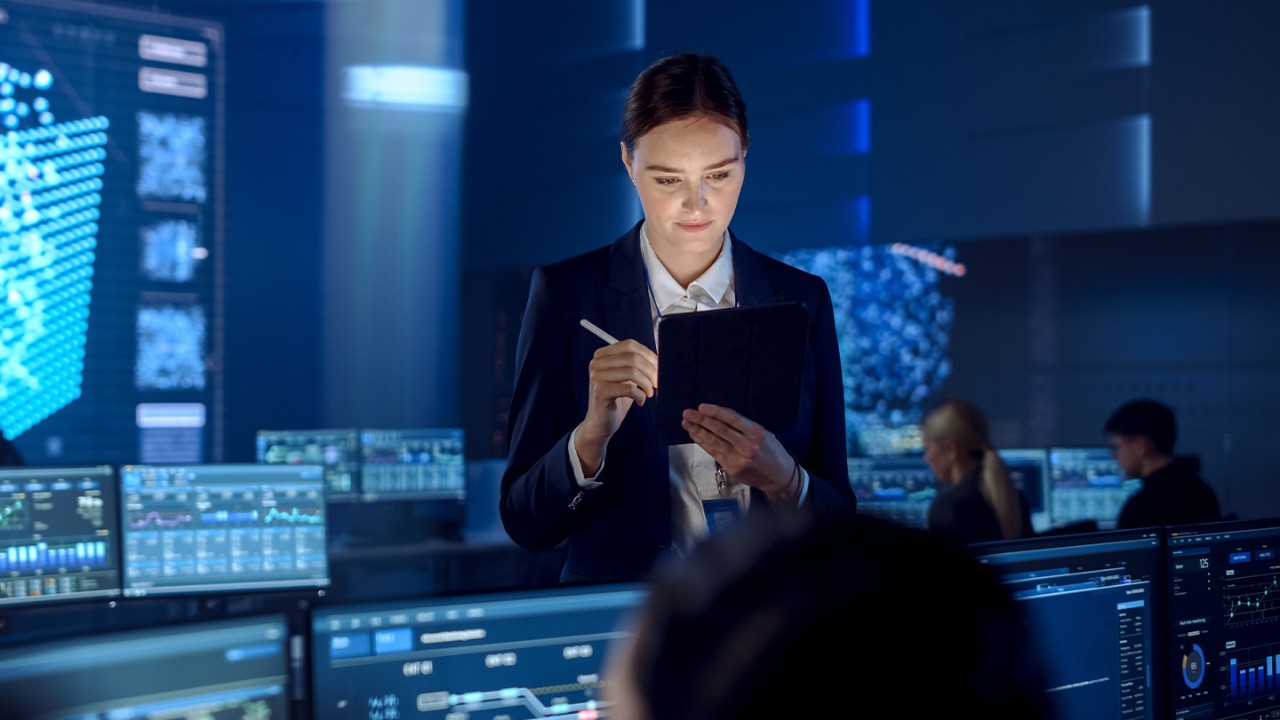Woman works on a tablet while standing in a mission control room