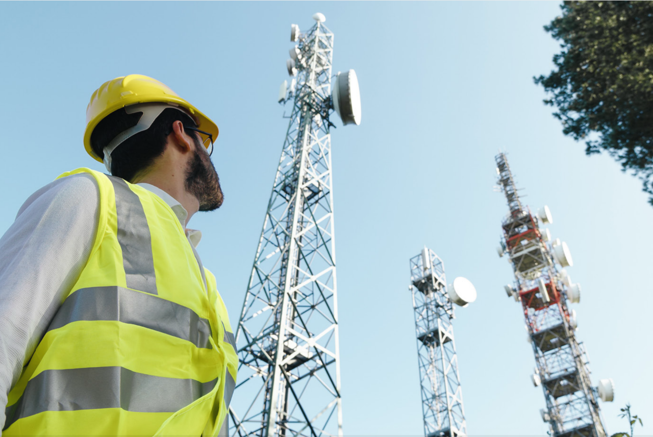 man in hardhat looking up at signal towers